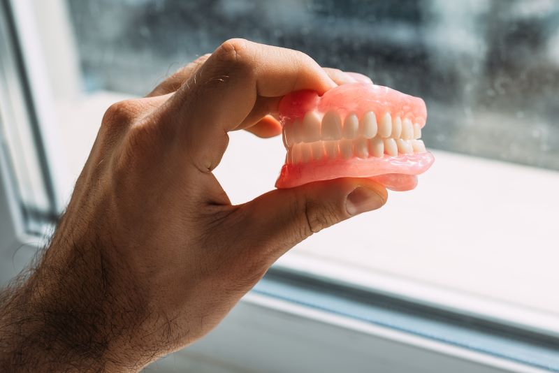 Man holding dentures against a window