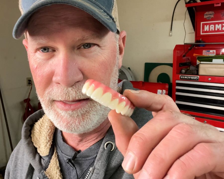 Patient holding up fake teeth to answer the question, do dental implants feel normal