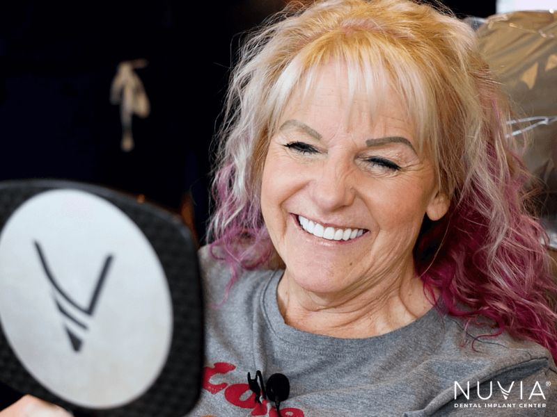 Woman with new teeth from her prosthodontist in tampa smiling in the mirror
