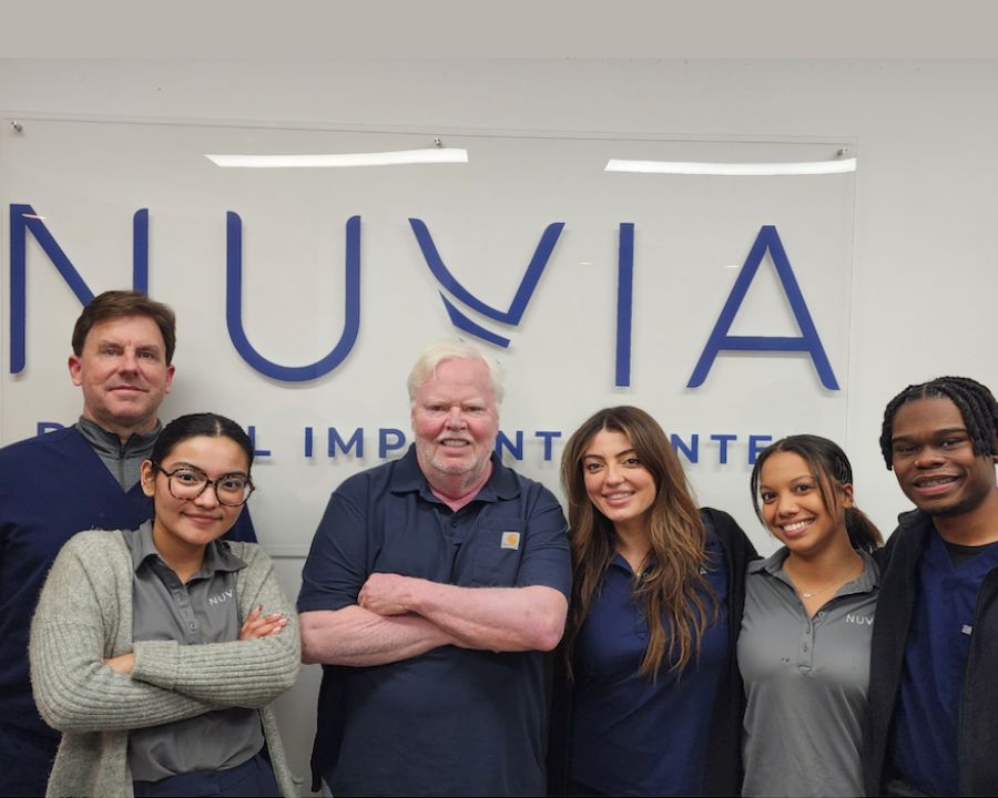 A group of people smiling in front of a nuvia dental implant sign